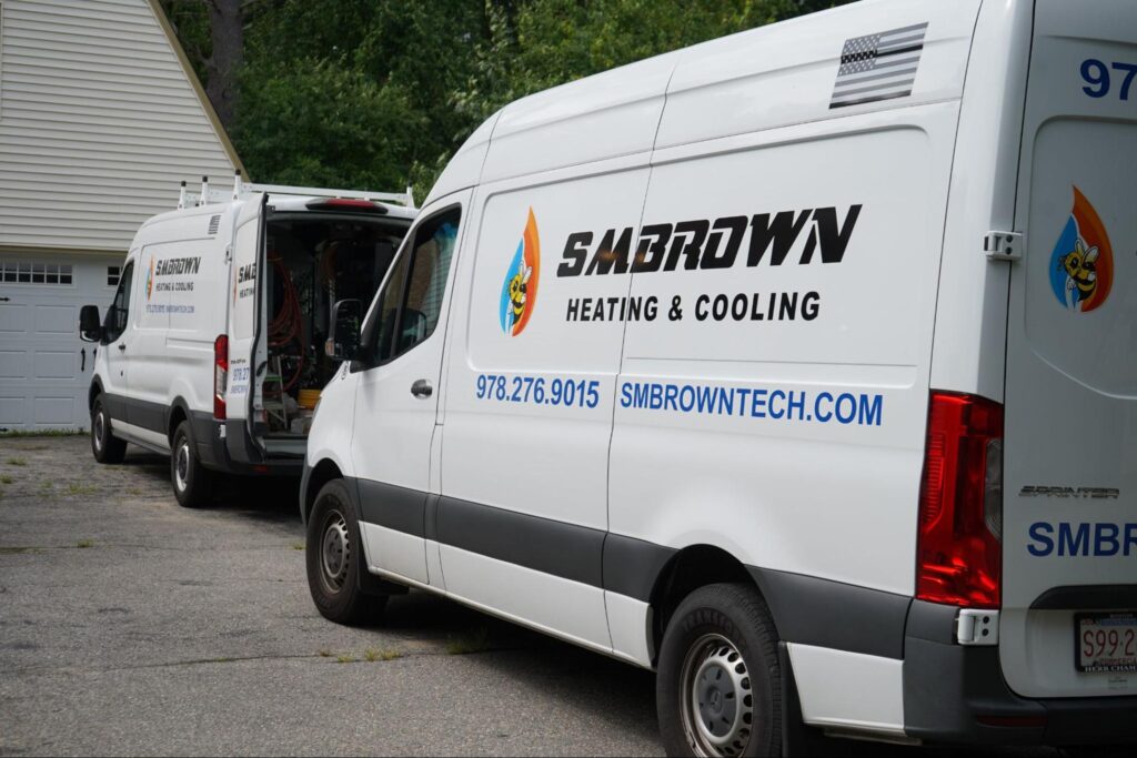 SM-Brown-Residential-Cooling-truck Two white vans labeled "SMBROWN Heating & Cooling" are parked on a driveway, their presence a testament to top-notch Residential Cooling services. The rear doors of one van are open, ready to serve the needs of the town's eager residents.